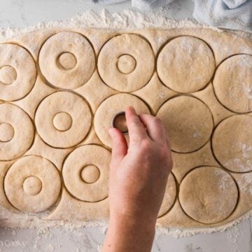 Hand pressing down mini circles in the middle of the donuts to cut out a hole.