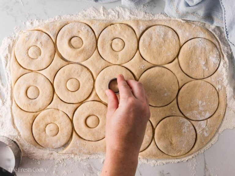 Hand pressing down mini circles in the middle of the donuts to cut out a hole.