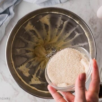 Sugar being added to the creamed butter in a mixing bowl.