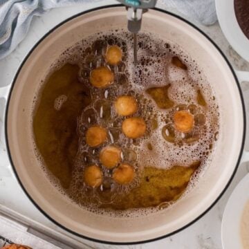 Donut holes frying in a large pot of oil.