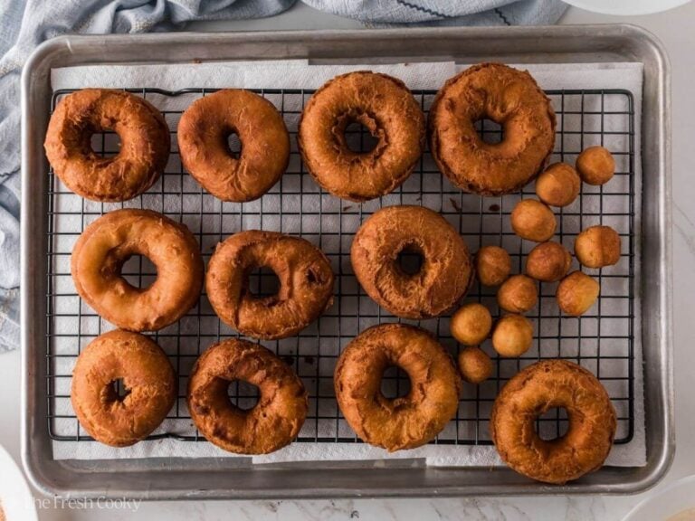Golden brown donuts on a wire rack on a sheet pan.