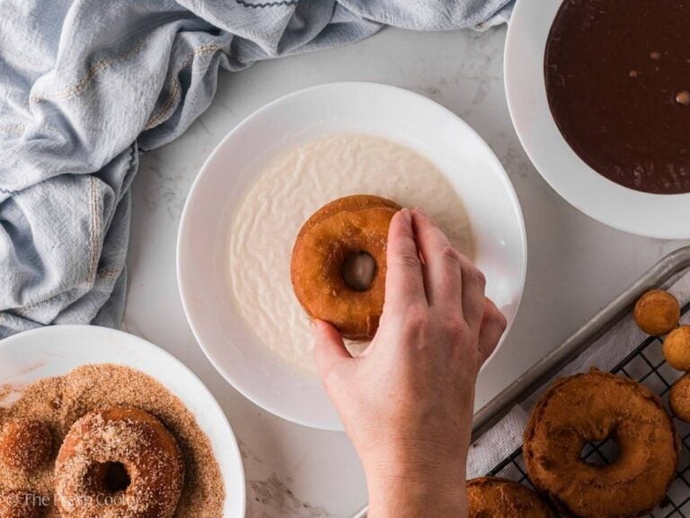 Hand dipping a donuts into glaze.