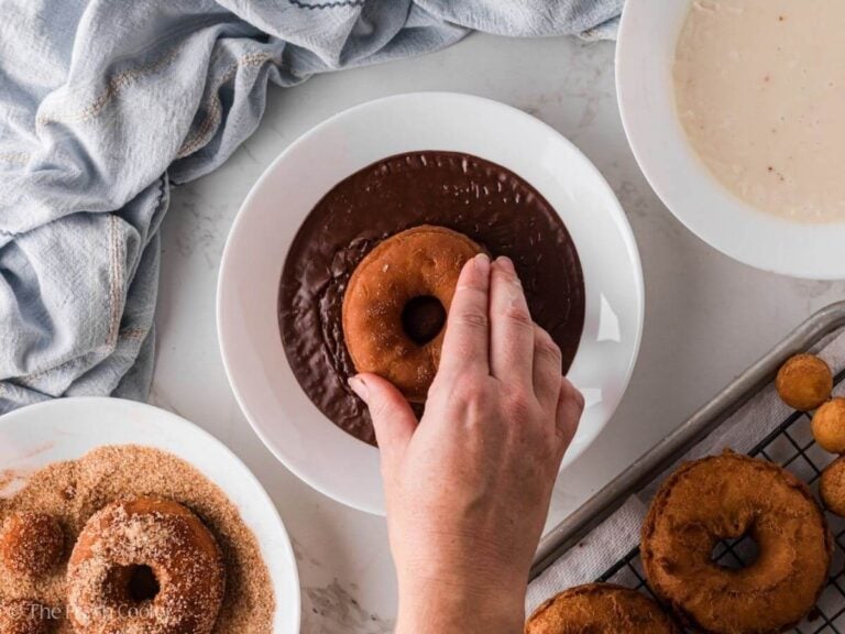 Hand dipping a donut into chocolate glaze.