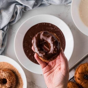 Hand holding a donut that has been dipped in chocolate glaze.