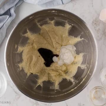 Sour cream and vanilla extract added to the creamed butter and sugar in a mixing bowl.