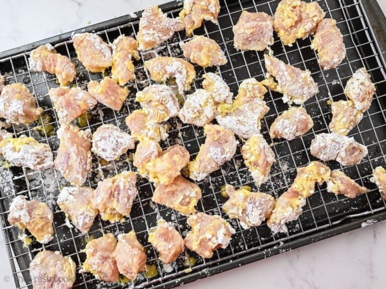 Dredged pieces of chicken on a sheet pan lined with a wire rack.