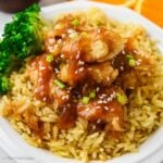 Rice with orange chicken on top on a plate.