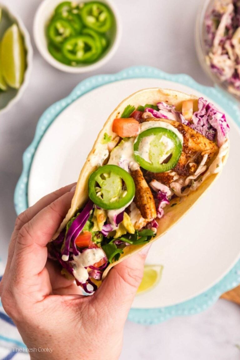 Hand holding a tilapia fish taco hovering over a plate.