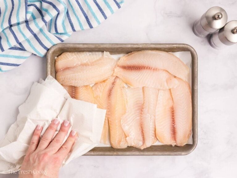 Hand using paper towels to dab the tilapia fillets dry.
