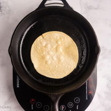 Corn tortilla placed on a cast iron skillet to char.