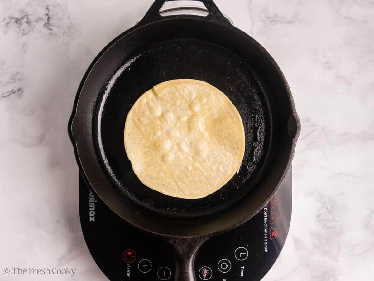Corn tortilla placed on a cast iron skillet to char.