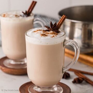 Chai tea lattes in glass mugs, both garnished with cinnamon and star anise.