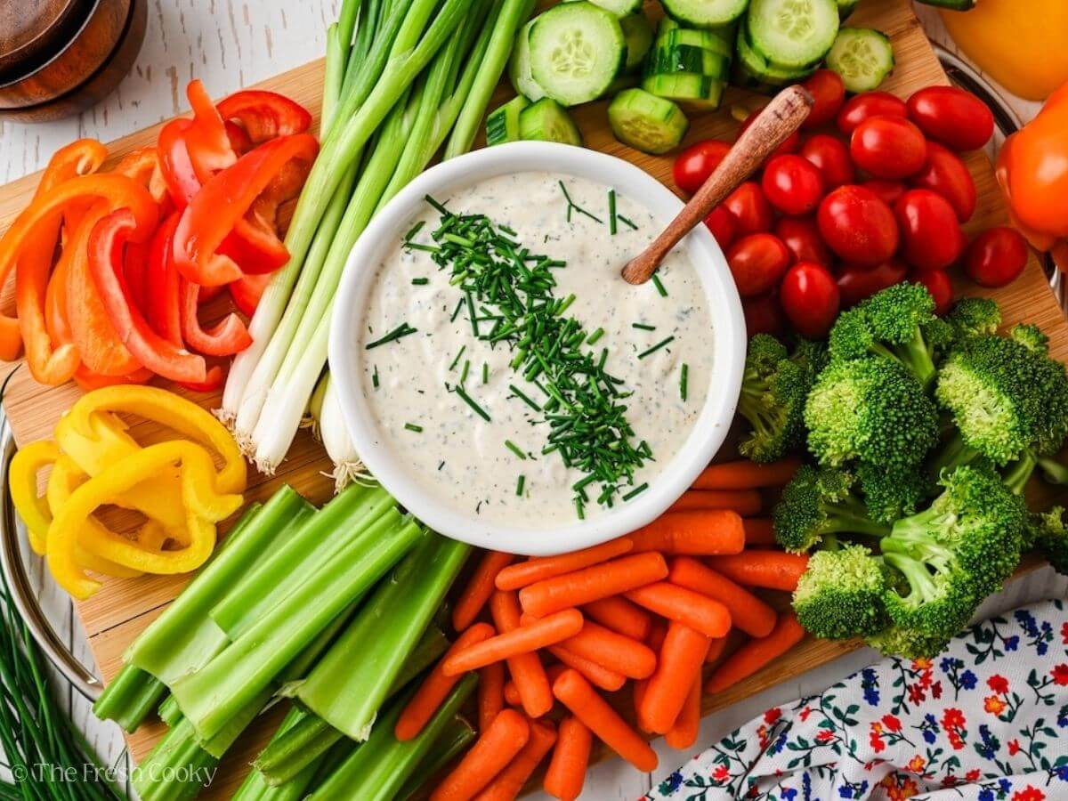 Bowl of crudite veggie dip on a cutting board loaded with fresh vegetables for dipping.
