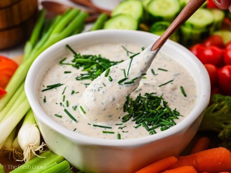 A wooden spoon dipping into the veggie dip, surrounded by vegetables.