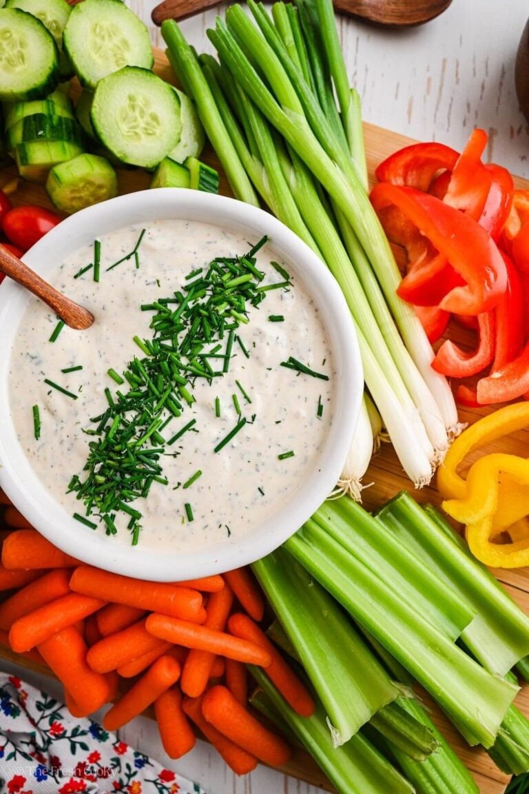 Veggie dip in a small white bowl surrounded by fresh, vibrant raw vegetables.