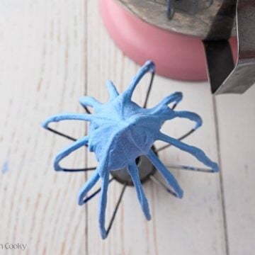 Whip attachment with blue whipped cream on it.