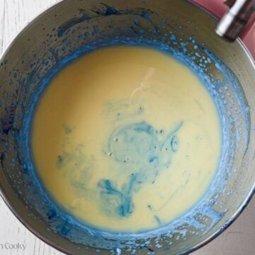 Condensed milk added to the blue whipped cream in a bowl.