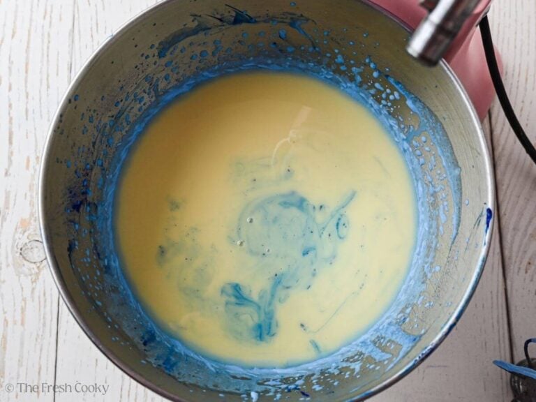 Condensed milk added to the blue whipped cream in a bowl.