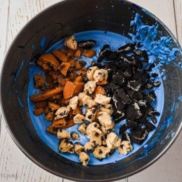 Bits of cookies added to the blue whipped cream mixture in a bowl.