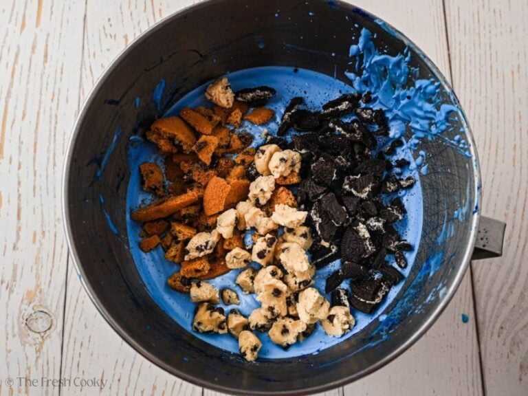 Bits of cookies added to the blue whipped cream mixture in a bowl.