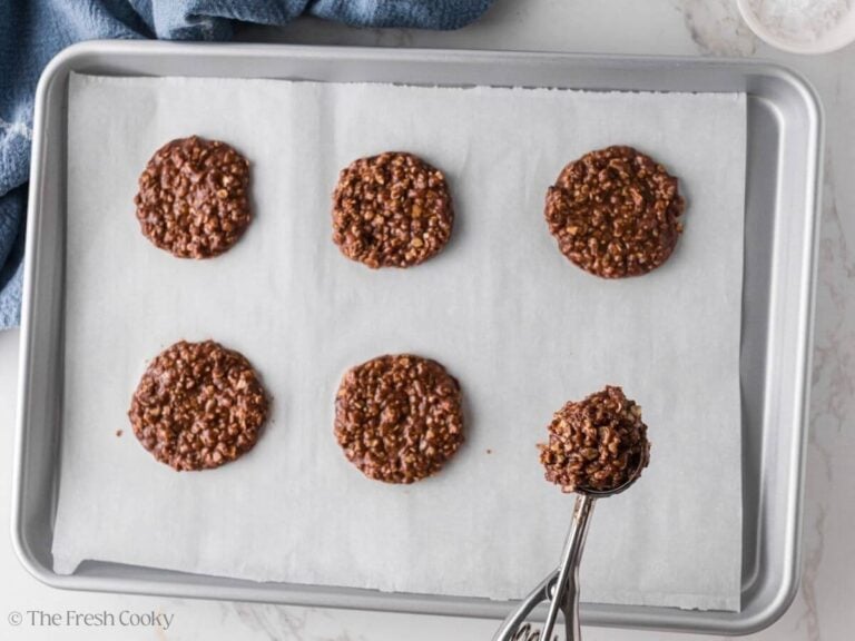 Chocolate oat cookies being dropped onto a parchment lined sheet pan.