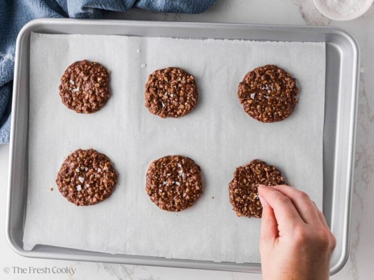 Hand sprinkling sea salt over the top of the chocolate oat cookies.