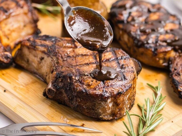Spooning a sauce over the top of a grilled pork chop on a wooden board.