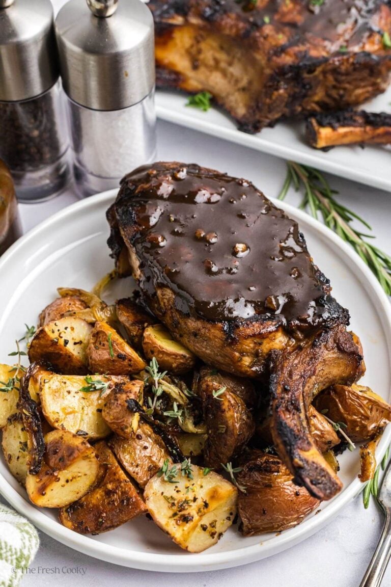 Marinated pork chop with sauce on top served on a plate with roasted potatoes.