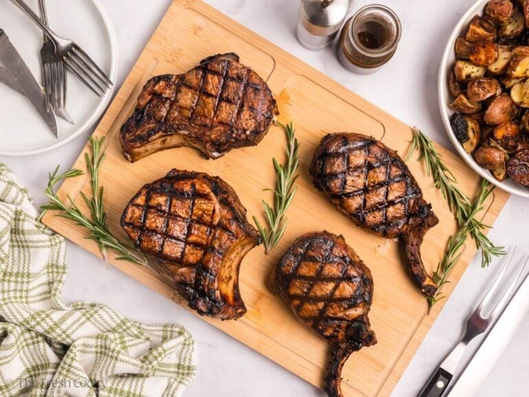 Four finished pork chops served on a wooden board.