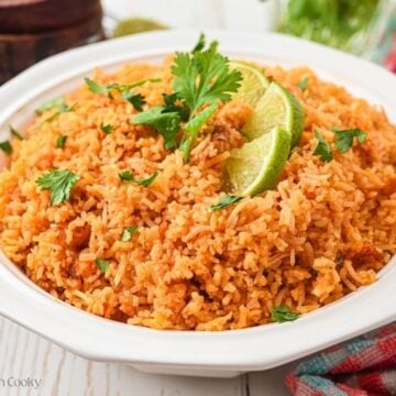 Large white serving bowl of Spanish rice, garnished with cilantro and lime slices.