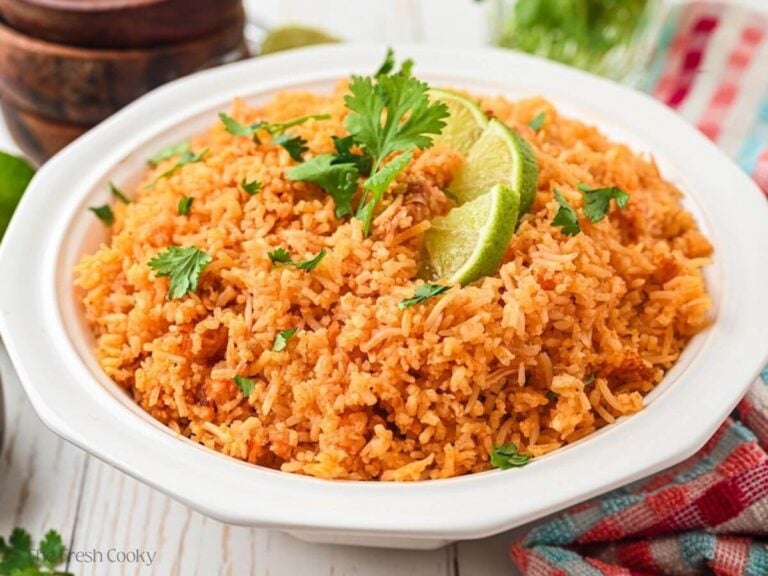 Large white serving bowl of Spanish rice, garnished with cilantro and lime slices.