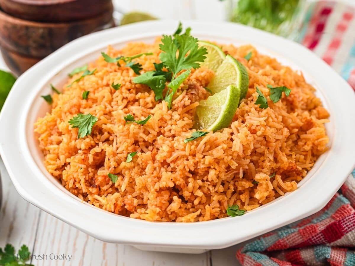 A pretty white bowl, filled with spanish rice, topped with lime wedges and cilantro.