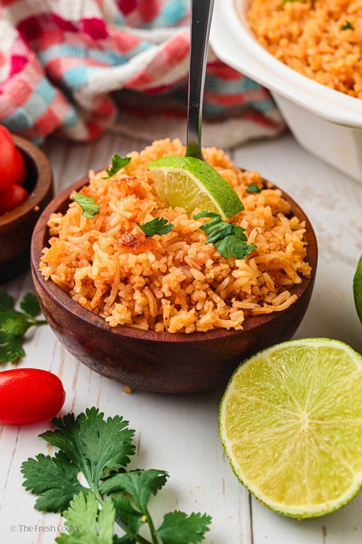 Small wooden bowl of Spanish rice with a spoon in the bowl, next to a half of a lime.