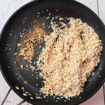 Toasted rice in a skillet with garlic and spices added.