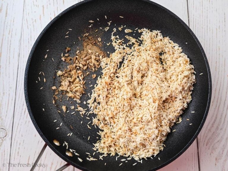 Toasted rice in a skillet with garlic and spices added.