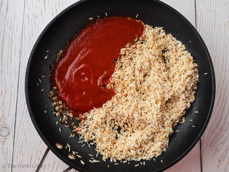 Tomato sauce added to the toasted rice in a skillet.