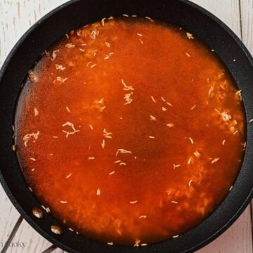 Broth added to the tomato sauce and rice in a skillet.