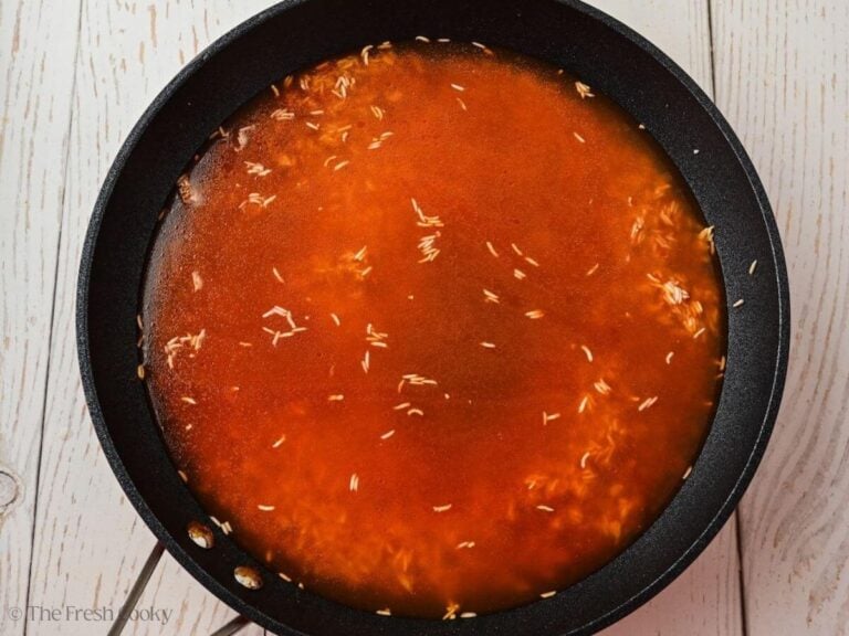 Broth added to the tomato sauce and rice in a skillet.