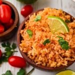 Close up of Spanish rice served in a wooden bowl next to a bowl of tomatoes.