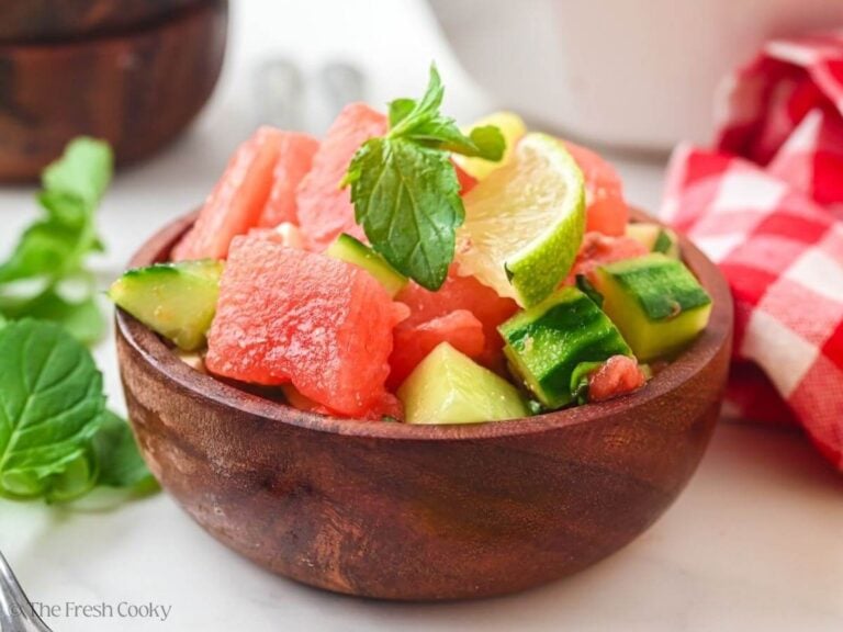 Side view of a small wooden bowl of watermelon cucumber salad garnished with mint.