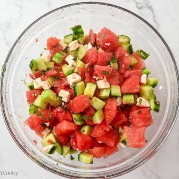 Watermelon cucumber salad all mized together with the dressing in a large bowl.