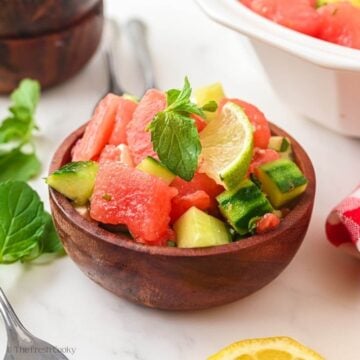 Side view of watermelon cucumber salad in a small wooden bowl.