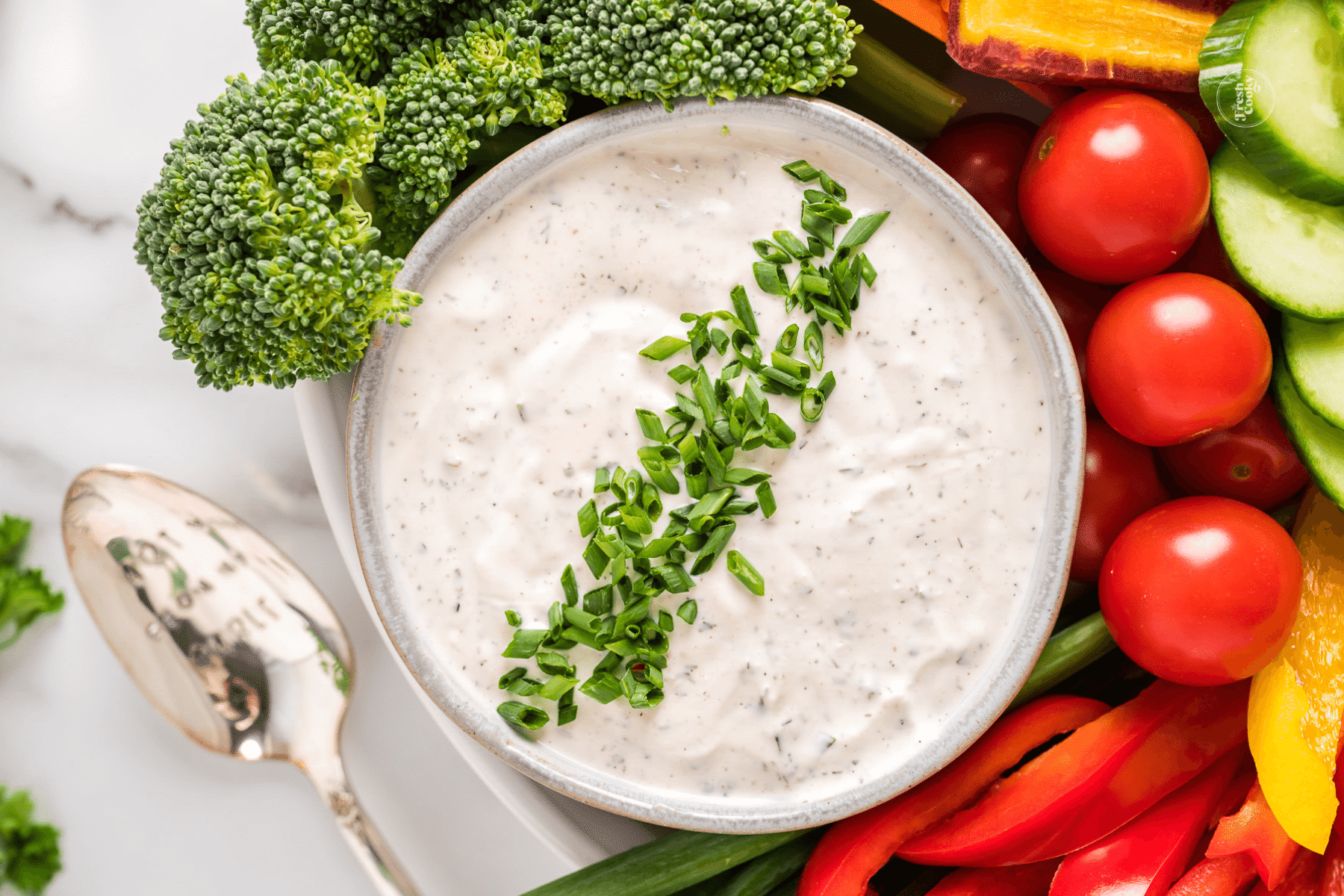 Lovely veggie dip in rustic bowl garnished with chopped chives with fresh veggies surrounding the dip.