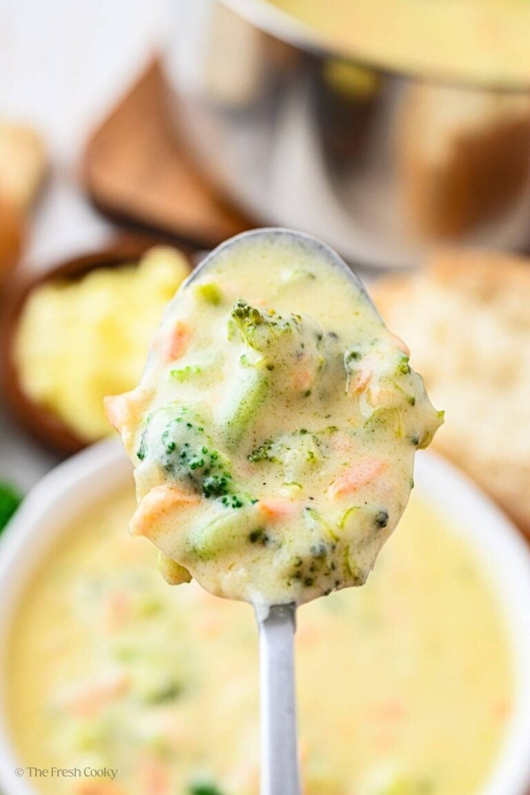 Overhead shot of a spoonful of broccoli cheese soup hovering over a bowl.