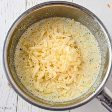 Shredded cheese added to the broccoli cheese soup in a pot.