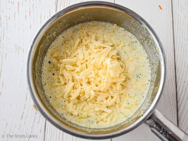 Shredded cheese added to the broccoli cheese soup in a pot.