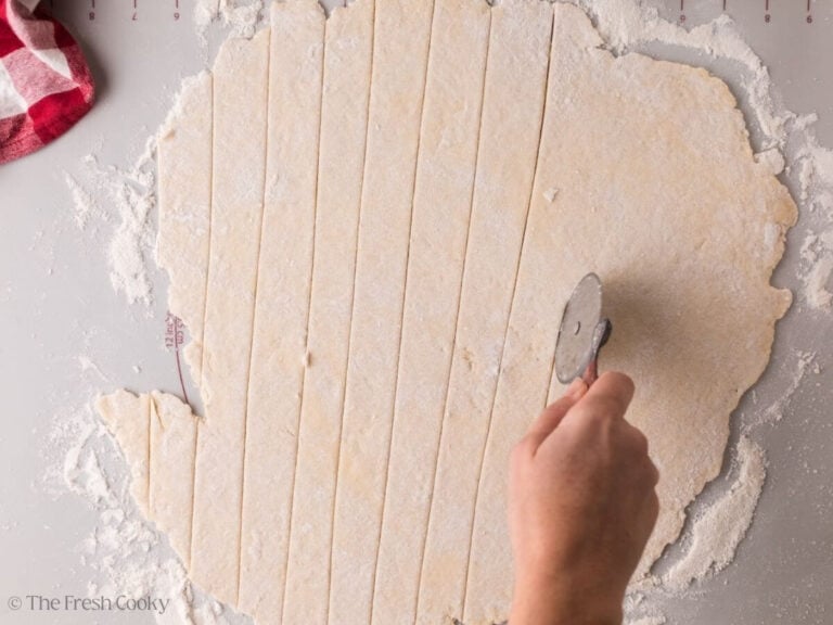 Using a pizza cutter to slice the dumpling dough into strips.