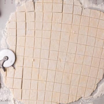 Using a pizza cutter to slice the dumplings into squares.