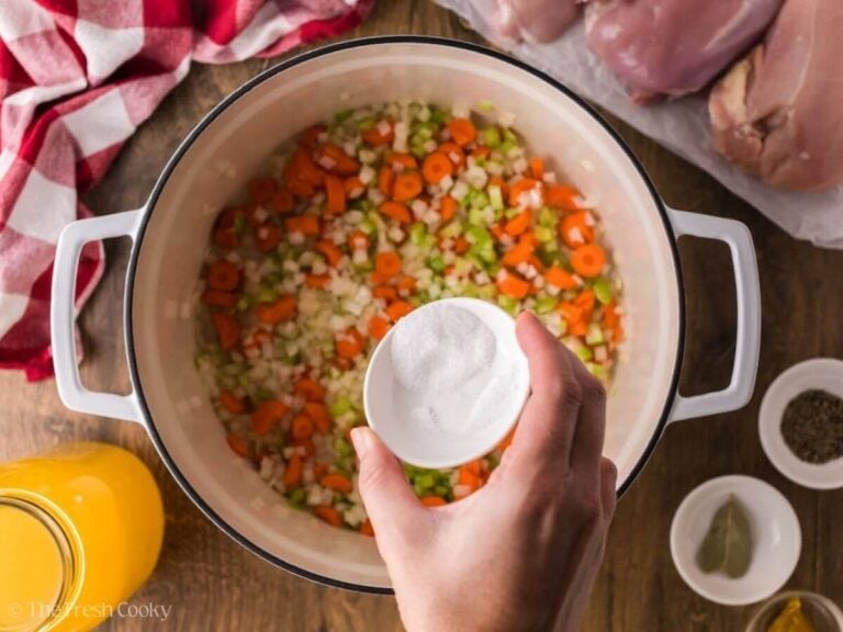 Adding salt to veggies in a pot.
