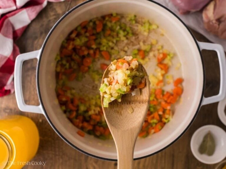 Wooden spoon with sauteed onions, carrots and celery on it.